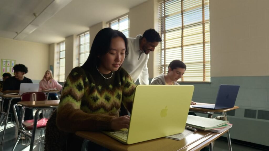 young woman seated at a classroom desk using a MacBook Neo